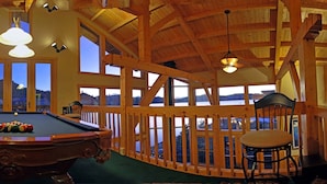 A pool table in a room with wooden beams and large windows, offering views of a lake.