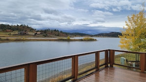 A wooden deck overlooking a calm lake with a distant view of houses and hills.