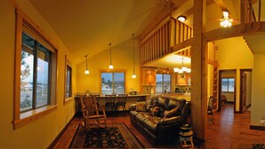 A spacious living room with a leather sofa, wooden flooring, and a large window.