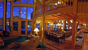 A spacious wooden interior with a dining area, a fireplace, and large windows offering a view of the outdoors.