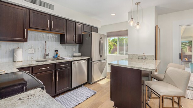 A modern kitchen with dark wood cabinets, stainless steel appliances, a granite countertop, and a bar area with a view. - Quiet Scottsdale Retreat ~ 3BR ~ FirePit, Garage, EV Charging ~ Prime Location (Scottsdale)