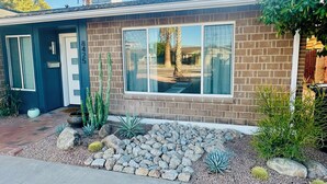 A two-story house with a brick facade, large windows, and a small garden with rocks and cacti. - Quiet Scottsdale Retreat ~ 3BR ~ FirePit, Garage, EV Charging ~ Prime Location (Scottsdale)