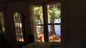 Une chambre à coucher avec un lit, une chaise et une fenêtre donnant sur un lac et des arbres.