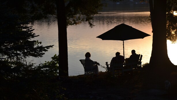 Une scène paisible au bord d’un lac, où l’on voit des personnes assises sous un parasol, entourées d’arbres.