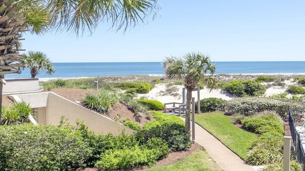 Un jardin aménagé avec des allées, des palmiers et une vue sur la plage et l’océan.