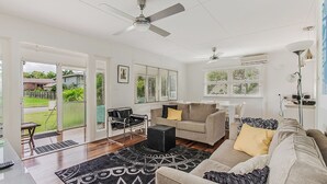 A spacious living room with a large window, a ceiling fan, and a black ottoman. - Charm & Character in the heart of Noosaville (Noosaville)