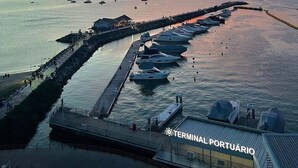 Een jachthaven aan het water met boten afgemeerd langs een steiger, een stadsachtergrond en een zonsondergang boven het water.