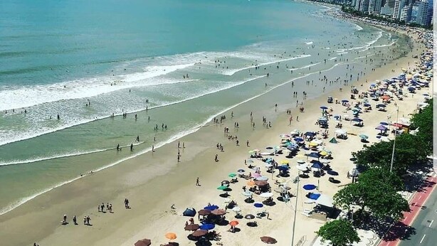 Een strand met parasols en mensen, met een stadsachtergrond en een weg parallel aan het strand.