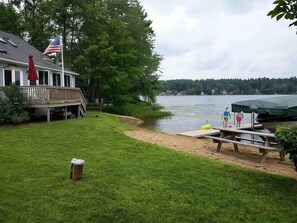 A lakeside property with a grassy yard, a dock, and a covered seating area. - ~Baboosic Lake Waterfront Rental~ (Amherst)