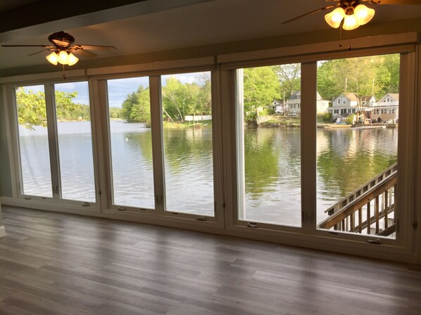 A room with large windows overlooking a lake, a ceiling fan, and a wooden deck. - ~Baboosic Lake Waterfront Rental~ (Amherst)