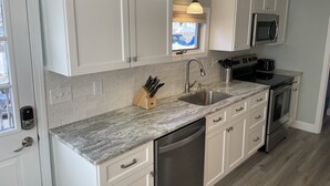 A modern kitchen with white cabinets, a granite countertop, stainless steel appliances, and a window with a view.