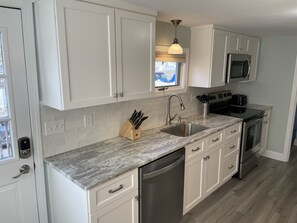 A modern kitchen with white cabinets, a granite countertop, stainless steel appliances, and a window with a view. - ~Baboosic Lake Waterfront Rental~ (Amherst)