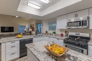 Una cocina moderna con encimeras de granito, electrodomésticos de acero inoxidable y un comedor con televisor de pantalla plana.