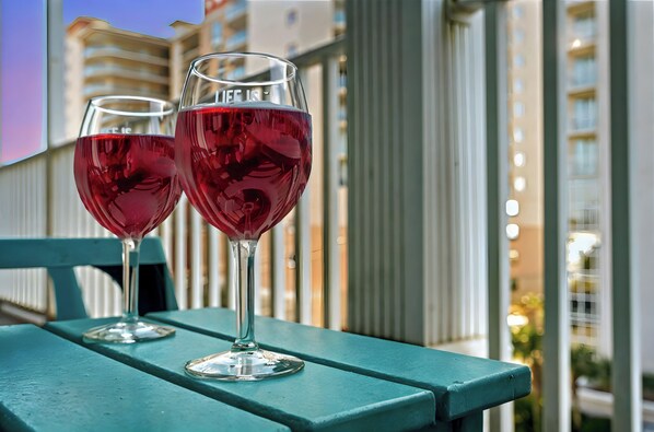 Deux verres à vin sont posés sur un banc de couleur turquoise, avec une vue sur la ville en arrière-plan.