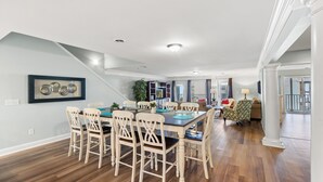 Un comedor amplio con una mesa larga y numerosas sillas, una escalera que conduce a un nivel superior, y vistas al exterior a través de amplios ventanales.