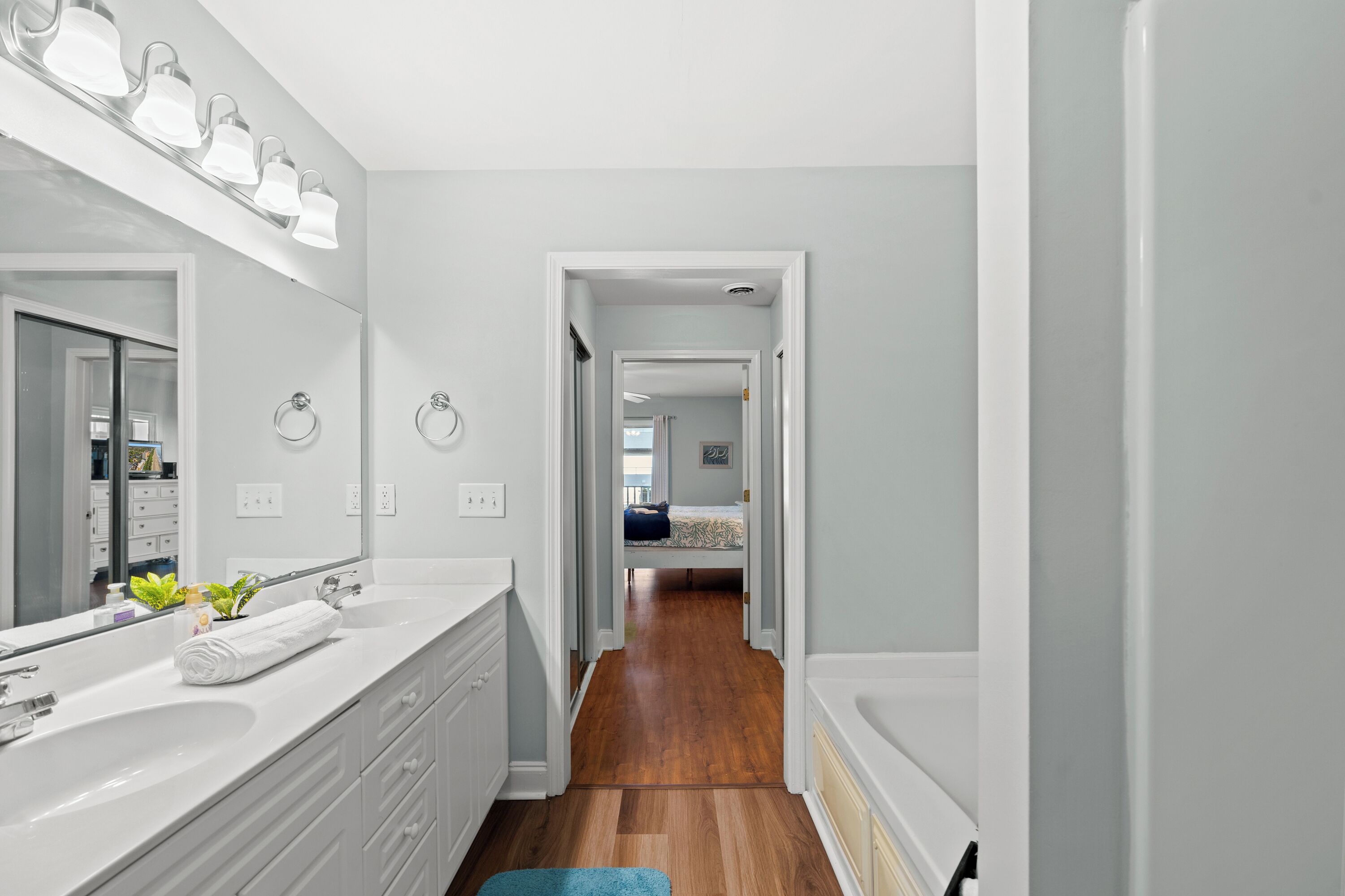 A modern bathroom with a large mirror, white fixtures, and a wooden floor.