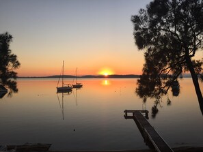 Tyyni järvi auringonlaskun aikaan, rannalla laituri ja järvellä purjeveneitä.