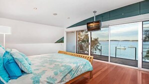 Un dormitorio con cama, televisión y un ventanal con vistas al agua.