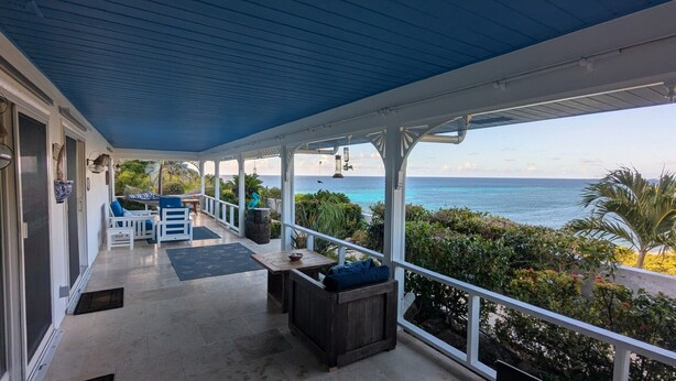 A covered outdoor area with a view of the ocean, featuring a seating area with chairs and a table. - Gorgeous Private Pool And Ocean Views Await! (Christiansted)