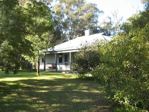 Une maison avec un porche, entourée d’arbres et d’herbe.