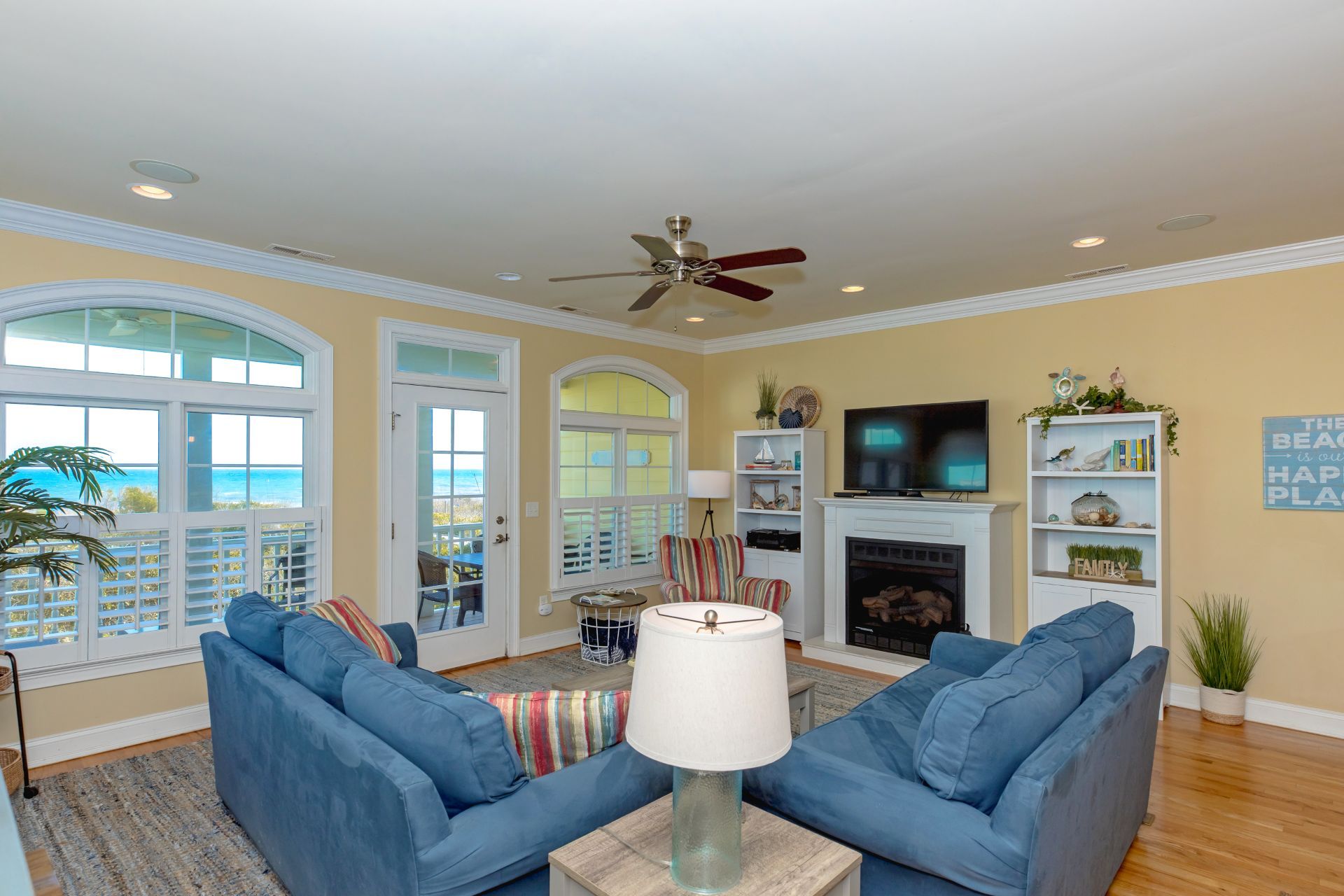 A living room with a fireplace, a television, and a view of the ocean through large windows.