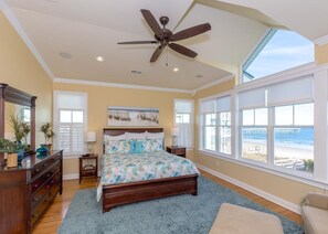A bedroom with a large bed, a ceiling fan, a dresser, a nightstand, and a view of the beach. - The Lazy Loggerhead - 4 BR Duplex w/ Great Covered Porch! (Topsail Beach)