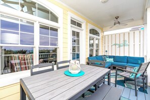 A covered outdoor seating area with a wooden table, blue sofa, and a ceiling fan. - The Lazy Loggerhead - 4 BR Duplex w/ Great Covered Porch! (Topsail Beach)