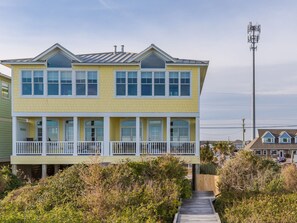 A two-story house with a balcony, surrounded by vegetation. - The Lazy Loggerhead - 4 BR Duplex w/ Great Covered Porch! (Topsail Beach)