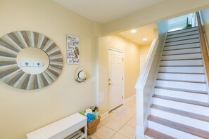A hallway with a staircase, a white door, a wall-mounted mirror, and a wall decoration. - The Lazy Loggerhead - 4 BR Duplex w/ Great Covered Porch! (Topsail Beach)