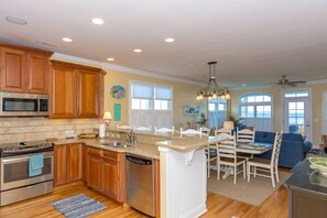 A kitchen with wooden cabinets, stainless steel appliances, a central island, and a dining area with a blue couch. - The Lazy Loggerhead - 4 BR Duplex w/ Great Covered Porch! (Topsail Beach)