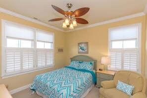 A bedroom with a bed, a chair, a nightstand, a ceiling fan, and a window with blinds. - The Lazy Loggerhead - 4 BR Duplex w/ Great Covered Porch! (Topsail Beach)