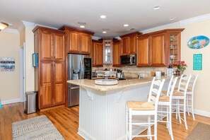 A kitchen with wooden cabinets, stainless steel appliances, a granite countertop, and a bar area with white chairs.