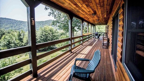Eine Holzterrasse mit Geländer, einem Stuhl und Blick auf eine bewaldete Landschaft.