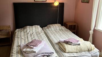 Una cama doble con cabecera negra, dos mesitas de noche, una silla pequeña y un cuadro en la pared.