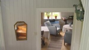 A narrow hallway leading to a living area with a sofa and a coffee table. A small table with a lamp and a decorative mirror is visible on the left.