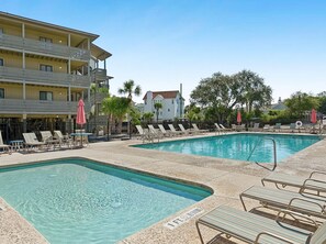 A hotel with a pool area featuring two rectangular pools, lounge chairs, and a building with balconies.