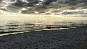 Een strand met een brede zandkust en uitzicht op de oceaan onder een bewolkte lucht.