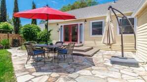 A patio with stone flooring, a table with chairs, a red umbrella, and a covered area with a beige umbrella.