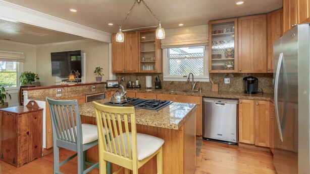 A modern kitchen with wooden cabinets, granite countertops, a stainless steel refrigerator, and a built-in dishwasher.
