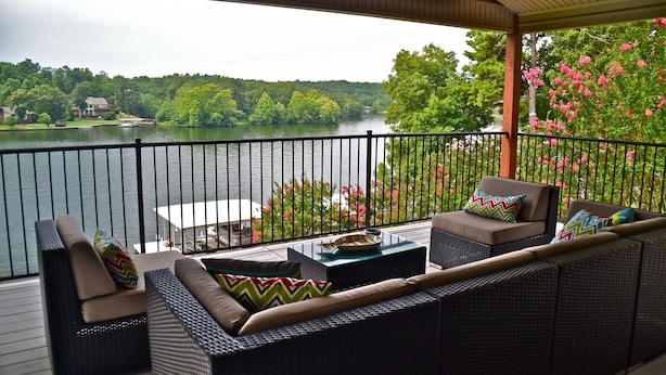 A covered outdoor seating area with wicker furniture and a view of a lake.