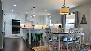 A modern kitchen with white cabinets, a central island, green bar stools, and a dining table with white chairs.