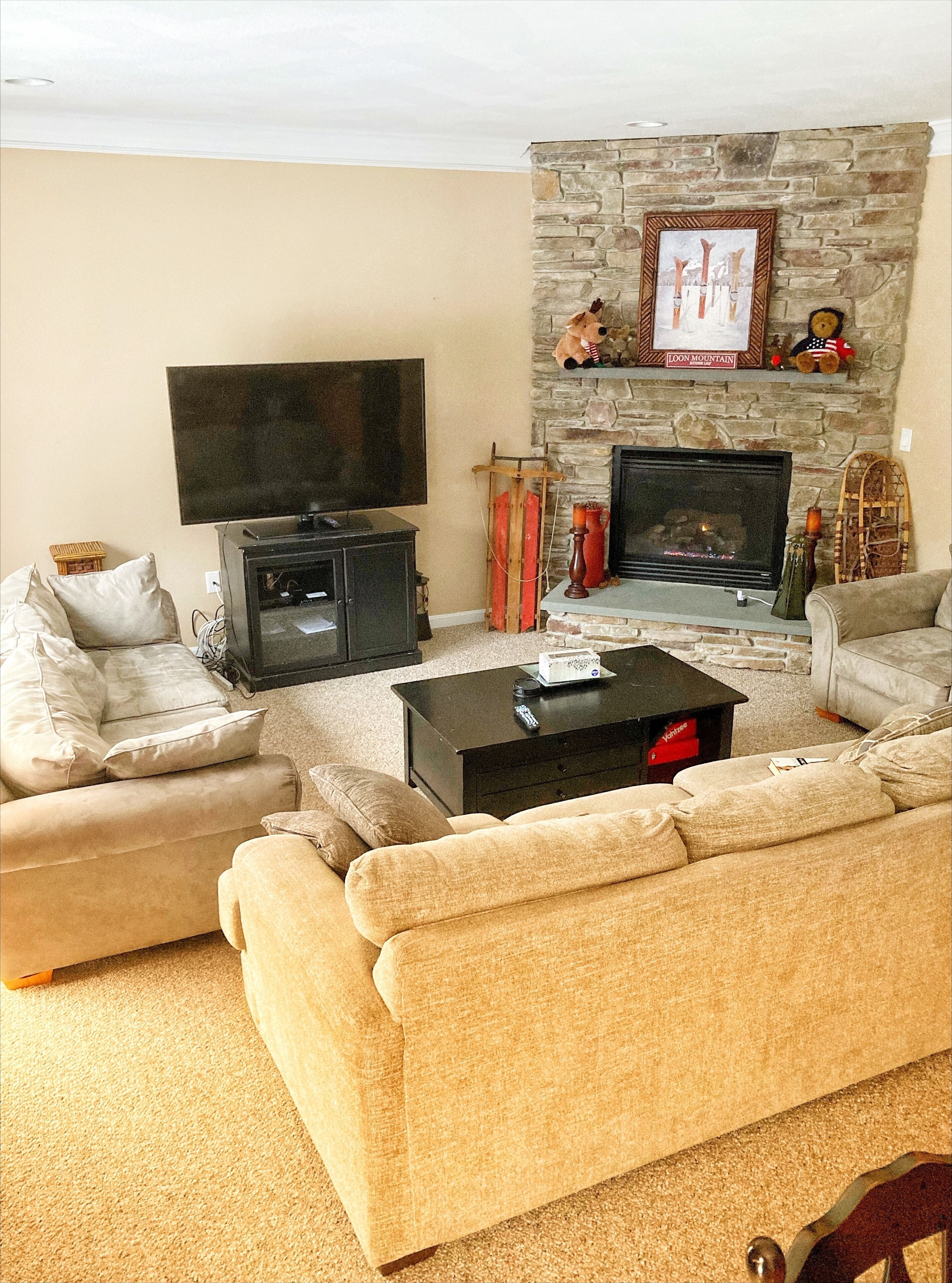 Una sala de estar con chimenea de piedra, un televisor de pantalla plana y un sofá grande color beige.