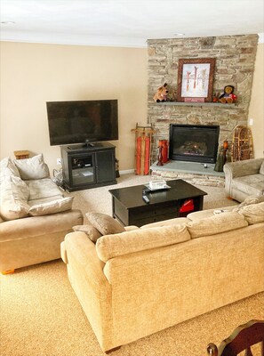 A living room with a stone fireplace, a flat-screen TV, and a large beige sofa.