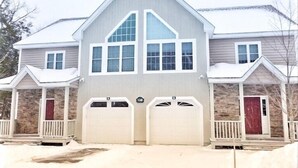 Une maison à deux étages, dotée d’un toit à pignon, de deux portes de garage et d’une façade en pierre.