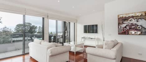 A spacious living room with two sofas, a coffee table, and a TV mounted on the wall.