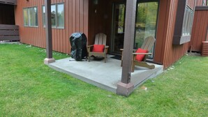 A wooden building with a covered porch, two Adirondack chairs with red cushions, and a barbecue grill. - Immaculate Updated Condo, 5 Minutes from Skiing!  (Wilson)