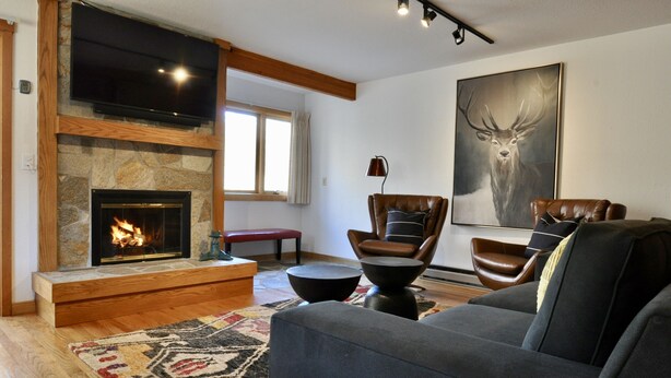 A living room with a stone fireplace, leather furniture, and a large deer painting. - Immaculate Updated Condo, 5 Minutes from Skiing!  (Wilson)