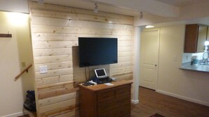Ein Zimmer mit Holzwandverkleidung, einem flachbildfernseher über einer Holzkommode, einem Laptop auf der Kommode und einem kleinen Teppich auf dem Boden.