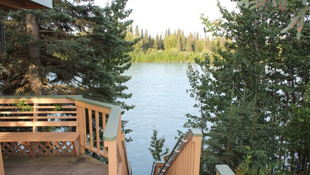Eine Holztreppe führt zu einer Terrasse mit Blick auf einen See, umgeben von Bäumen.