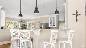 A kitchen with white bar stools, a large island, and pendant lighting. - Sand Castle | Heated Saltwater Pool, Game Room & Walk to Beach and Center Street (Folly Beach)